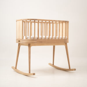Minimalistyczna drewniana kołyska Norah w kolorze jasnego jesionu na jednolitym tle.